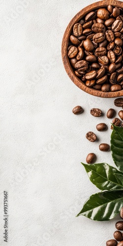 Coffee beans in a wooden bowl with green leaves on a light textured background. photo