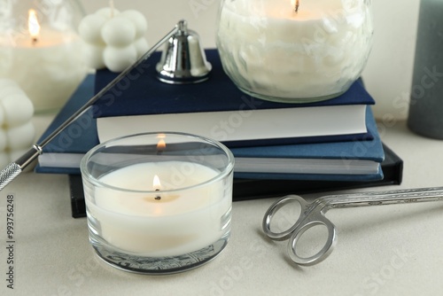 Beautiful burning candles, books, candle snuffer and wick trimmer on light table, closeup photo