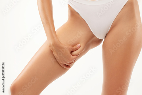 Slim woman touching inner thigh skin, enjoying result of slimming diet, standing isolated on white studio background, closeup photo