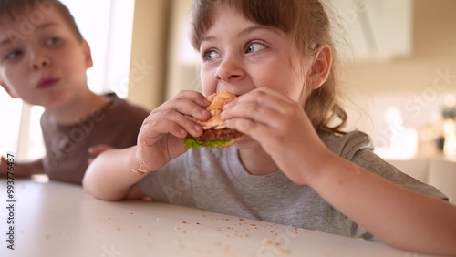 children eat burgers. fast food burger. a group of small children in the kitchen greedily eat fast food burgers. big family sun small kids having breakfast in the morning in the kitchen eating burger