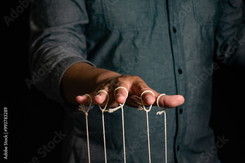 Close-up Of Man Controls The Puppet With Fingers. Man`s Hand Controls The Puppet With The Fingers Attached To Threads Against Black Background,Manipulation concept photo