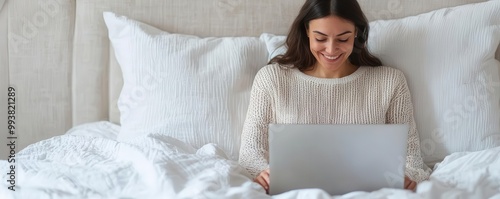 Person smiling while typing on a laptop in bed, feeling relaxed and comfortable while working from home   cozy remote work, home office vibes photo