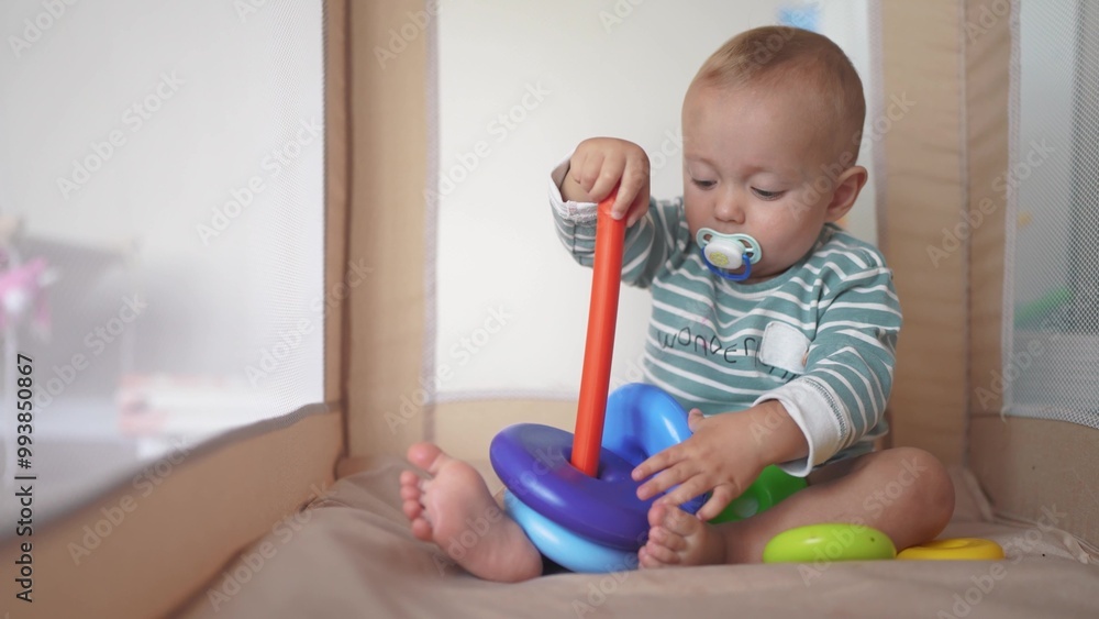 baby toddler plays with a toy pyramid sits in a crib arena. happy family kid dream concept. lifestyle baby toddler development of fine motor skills plays with pyramid rings in kindergarten baby toddler plays with a toy pyramid sits in a crib arena. happy family kid dream concept. lifestyle baby toddler development of fine motor skills plays with pyramid rings in kindergarten