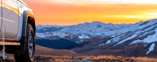 SUV on a rocky trail overlooking a mountain valley at dusk, sun setting behind snow-capped peaks, adventure and freedom photo