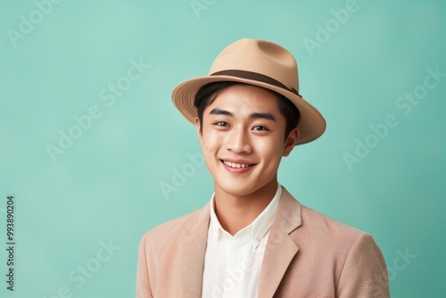 Portrait of a happy asian man in his 20s donning a classic fedora isolated in pastel or soft colors background