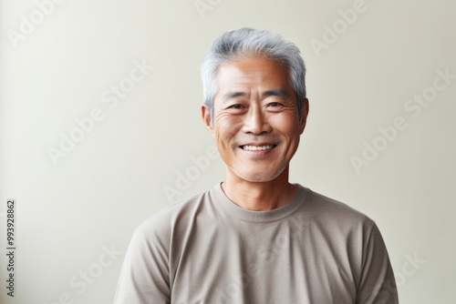 Portrait of a grinning asian man in his 60s donning a trendy cropped top isolated in minimalist or empty room background