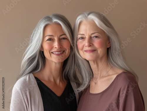 Two women, one in her thirties and one in her sixties, standing close together with soft smiles, against a neutral-toned background