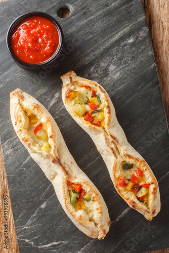 Pizza sorrentina tomato mozzarella and vegetables such as zucchini, tomato, pepper, artichoke closeup on the slate plate on the wooden table. Vertical top view from above photo