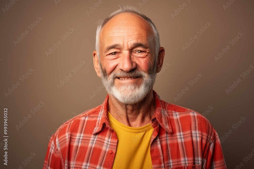 Portrait of a grinning man in his 70s dressed in a relaxed flannel shirt in front of solid color backdrop Portrait of a grinning man in his 70s dressed in a relaxed flannel shirt in front of solid color backdrop