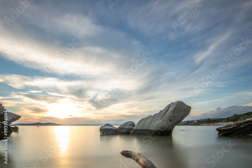 View through rocks on a sandy beach into the sunset. Landscape shot with a view to the horizon over the wide sea on the coast of Ouranoupoli, Thessaloniki, Central Macedonia, Greece photo