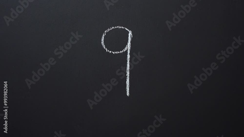 Hand writes the number 9 with white chalk on a black board
