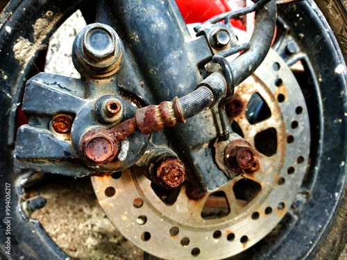 the front brake part of the motorbike is starting to rust. some bolts on the brake part are rusty and corroded. closeup for part motorcycle front brake, motorcycle front disc