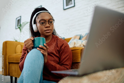 Fotografia Young black woman earing headphones while binge watching on laptop at home