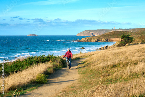 nice senior woman cycling with her electric mountain bike at the rocky emerald coast  of Brittany, France next to Cap Frehel