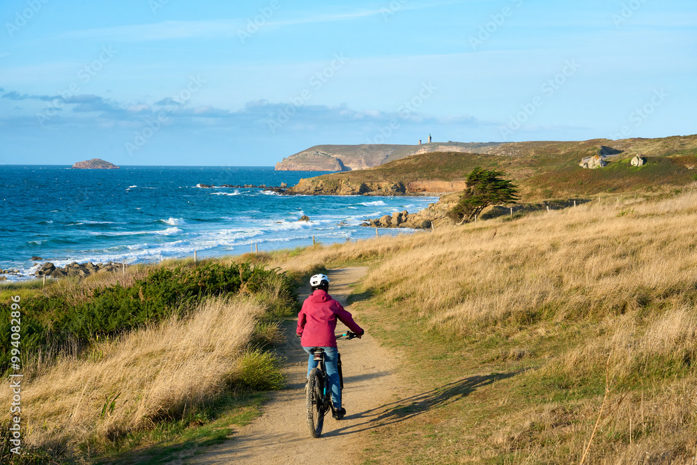 nice senior woman cycling with her electric mountain bike at the rocky emerald coast of Brittany, France next to Cap Frehel nice senior woman cycling with her electric mountain bike at the rocky emerald coast of Brittany, France next to Cap Frehel