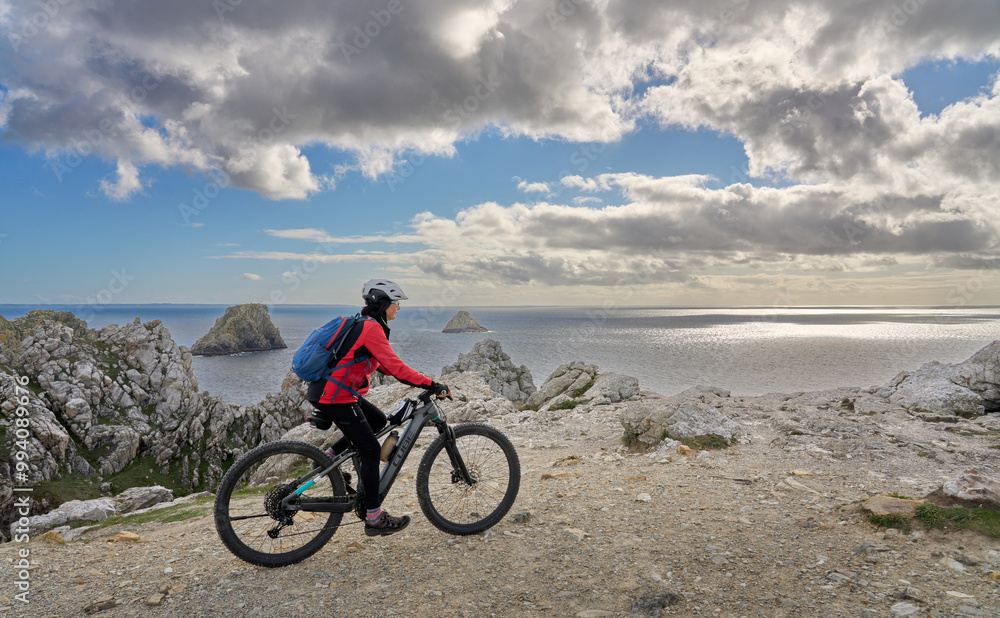 Fototapeta premium active senior woman cycling with her electric mountain bike along the wild coast of Finisterre in southern Brittany next to Camaret-sur-Mer, France