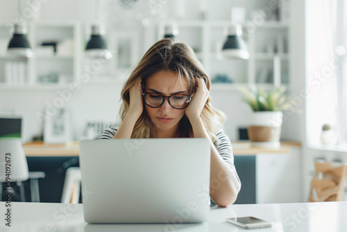 Stressed woman working on a laptop in a modern home office, illustrating the challenges of remote work, digital burnout, and the pressure of deadlines in a contemporary workspace