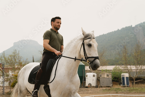 Portrait of a young rider on a white horse in an outdoor equestrian arena. The mountains behind. Equestrian Concept & Training