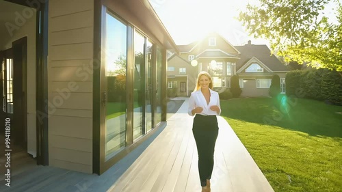 Female real estate agent walking outside a luxury modern home, sunny day, showcasing property, professional and stylish
