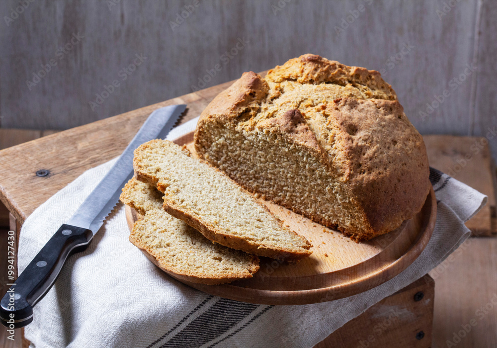 Homemade Irish soda bread cut into pieces and knife on wooden background.