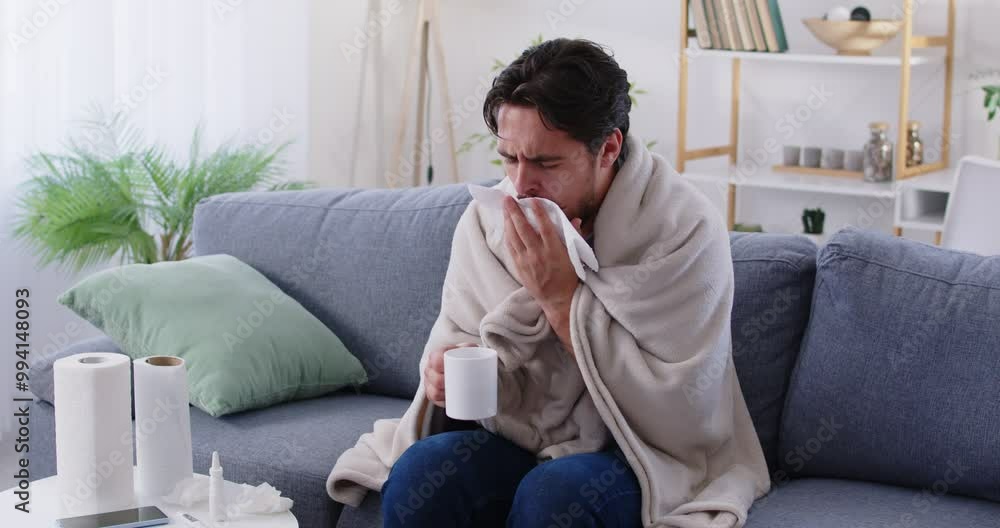 Portrait of a young unhealthy sick man sitting on sofa at home wrapped in a blanket and suffering from cough. Male person with seasonal flu. Healthcare and medicine concept. 4k video. Portrait of a young unhealthy sick man sitting on sofa at home wrapped in a blanket and suffering from cough. Male person with seasonal flu. Healthcare and medicine concept. 4k video.