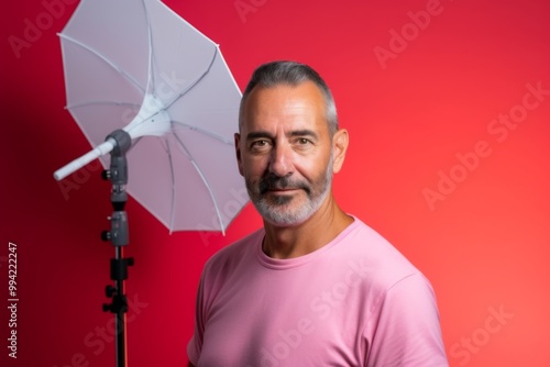 A man with a white umbrella stands in front of a red background