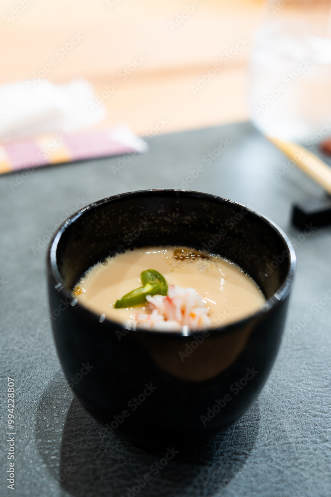 Closeup of a traditional Japanese steamed egg custard (chawanmushi) topped with crab meat and green garnish, served in a black bowl Closeup of a traditional Japanese steamed egg custard (chawanmushi) topped with crab meat and green garnish, served in a black bowl