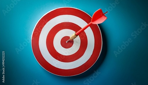 A red dart on target; an accurate dart on a red and white target; bullseye right on the target; red and white target with a dart on the bullseye; closeup view; low angle view; dart game