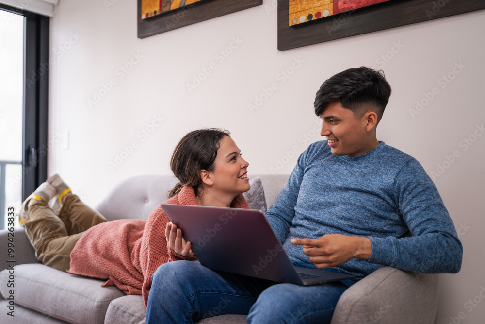 Newly married couple relaxing on sofa browsing internet on laptop Newly married couple relaxing on sofa browsing internet on laptop