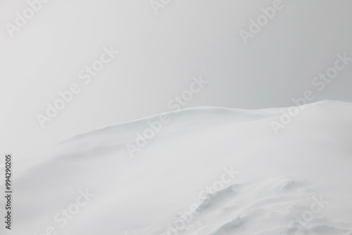 Minimalist Winter Landscape featuring Vast expanse of gently rolling Snowcovered Hills partially obscured by a soft mist. Solitary distant object adds focal point, creating serene and tranquil scene