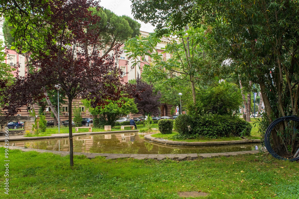 Lulishte Ismail Qemali Park in central Tirana, Albania. Located on the edge of the Blloku area, it's also known as Postblloku Park and is a small green oasis featuring a pond in the middle of this cap Lulishte Ismail Qemali Park in central Tirana, Albania. Located on the edge of the Blloku area, it's also known as Postblloku Park and is a small green oasis featuring a pond in the middle of this cap