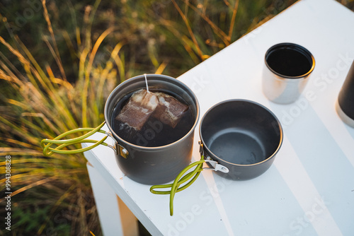 On a wellset table sits a pot of steaming hot tea, accompanied by an empty cup that awaits someone who wishes to pour a delightful beverage into it and savor a moment of relaxation photo