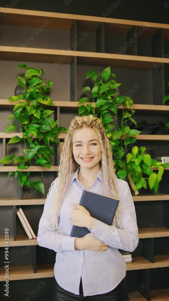 A Smiling, Young Woman with dreadlocks in a Modern Office Exudes Confidence and Creativity as She Holds a Notebook While Engaging in Professional Work, vertical video A Smiling, Young Woman with dreadlocks in a Modern Office Exudes Confidence and Creativity as She Holds a Notebook While Engaging in Professional Work, vertical video