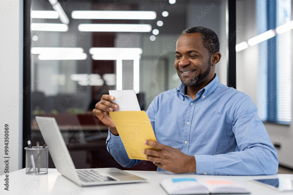 Male office worker opens mail envelope at desk, smiling at good news. Workplace scene with laptop, showcasing productivity, success, and satisfaction in office. Represents professional achievement. Male office worker opens mail envelope at desk, smiling at good news. Workplace scene with laptop, showcasing productivity, success, and satisfaction in office. Represents professional achievement.