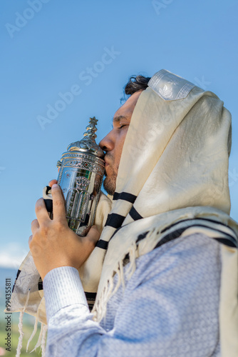 Young Jewish Man in Tallit Kissing a Sefer Torah in Celebration of Simchat Torah. vertical photo