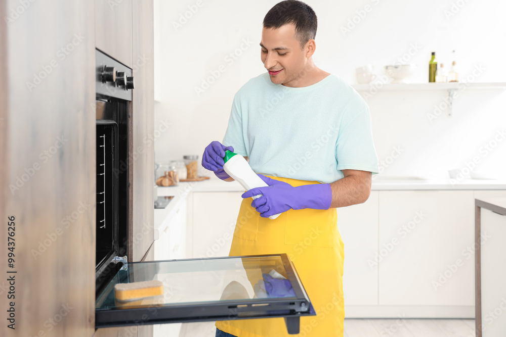 Young man with sponge and detergent cleaning oven in kitchen Young man with sponge and detergent cleaning oven in kitchen