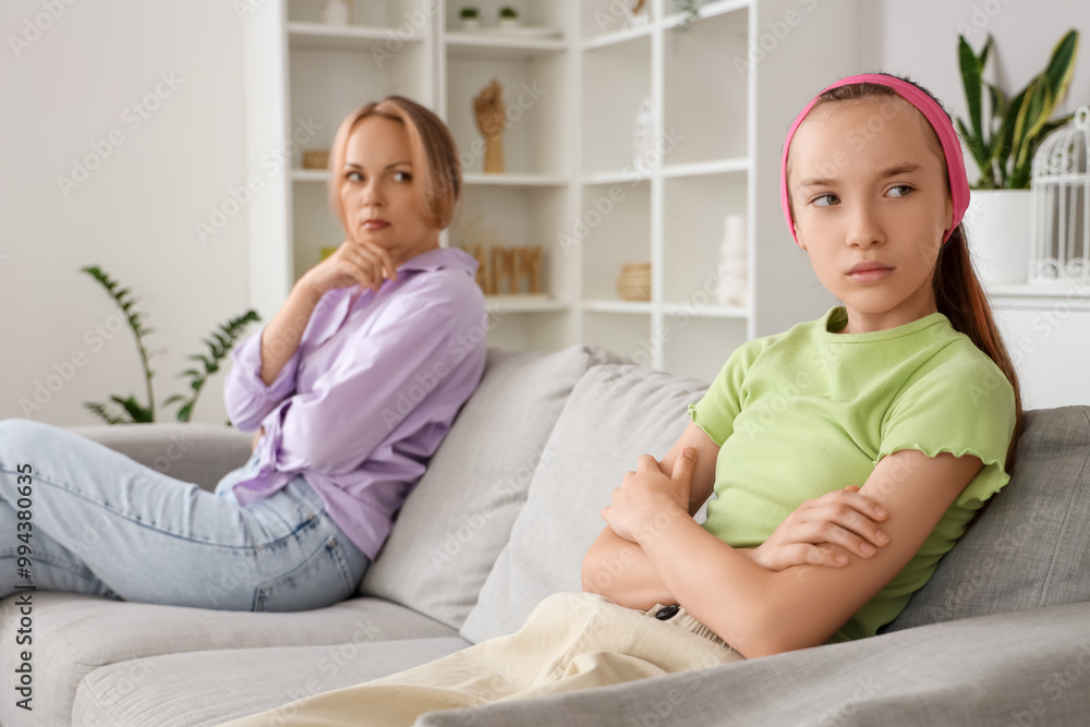 Sad teenage girl sitting on sofa after quarrel with her mother at home. Family difficulties concept Sad teenage girl sitting on sofa after quarrel with her mother at home. Family difficulties concept