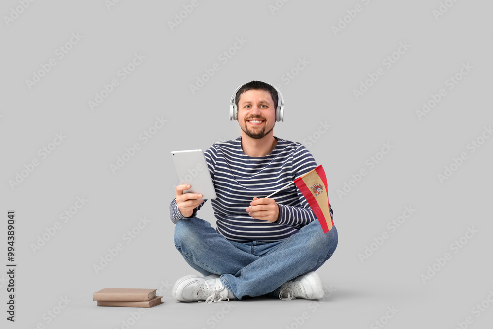 Handsome man in headphones with tablet computer and flag of Spain learning language online on light background Handsome man in headphones with tablet computer and flag of Spain learning language online on light background