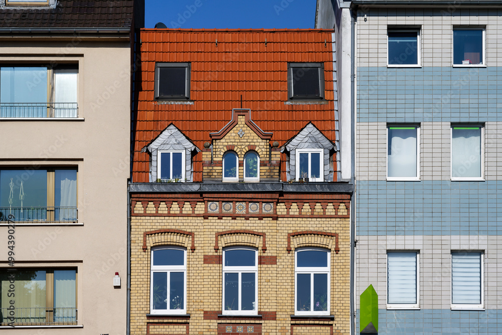 Naklejka premium a pretty old small founder's era house made of yellow and red brick, squeezed into simple post-war buildings in Cologne Ehrenfeld