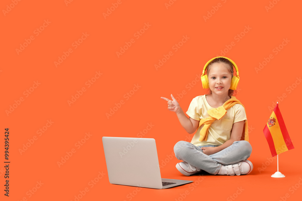 Little girl with Spanish flag and laptop pointing at something on orange background Little girl with Spanish flag and laptop pointing at something on orange background
