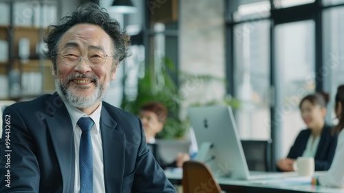 A cheerful elderly man in a suit, with a bright smile, sits in a modern office setting, radiating happiness and professional fulfillment.