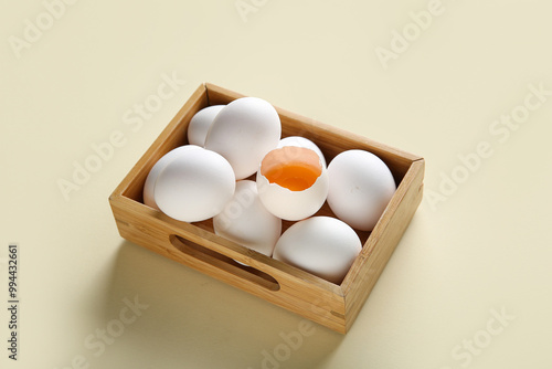 Wooden box with raw chicken eggs on beige background