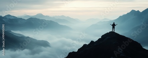 Person standing triumphantly on a mountain peak overlooking misty valleys at ...
