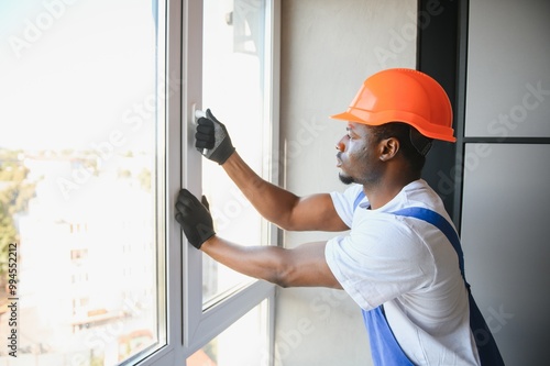 Workman in overalls installing or adjusting plastic windows in the living room at home