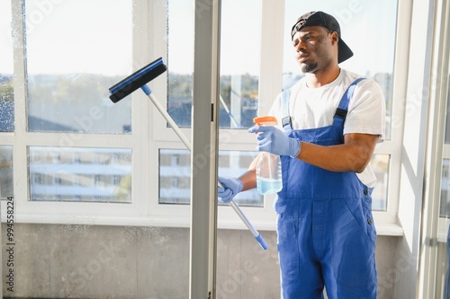 Wallpaper Mural African Male professional cleaning service worker in overalls cleans the windows and shop windows of a store with special equipment Torontodigital.ca