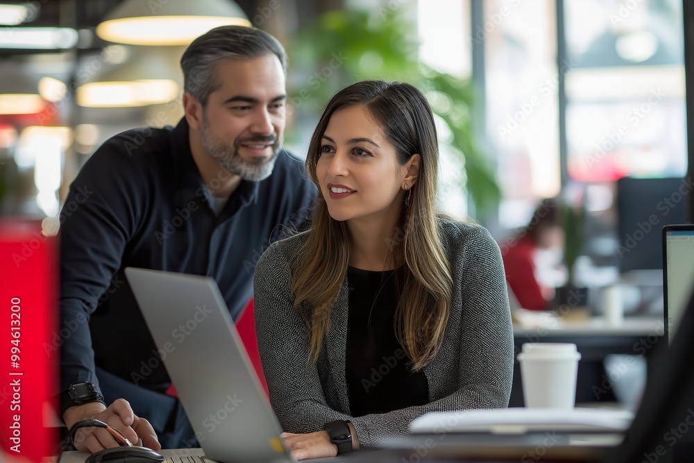 A young Latina woman in professional attire collaborates with a colleague at a modern office workspace, focusing on a laptop during a busy workday A young Latina woman in professional attire collaborates with a colleague at a modern office workspace, focusing on a laptop during a busy workday