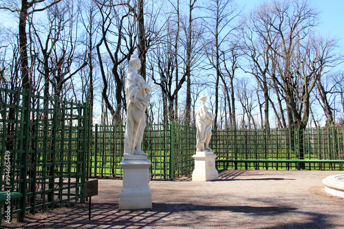 Two marble statues stand in a garden pavilion surrounded by lattice green fences and bare trees, creating a serene and artistic atmosphere on a sunny day photo