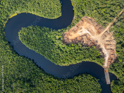 Aerial drone view of Amazon rainforest log storage area: sustainable wood harvesting next a river amidst the dense jungle canopy