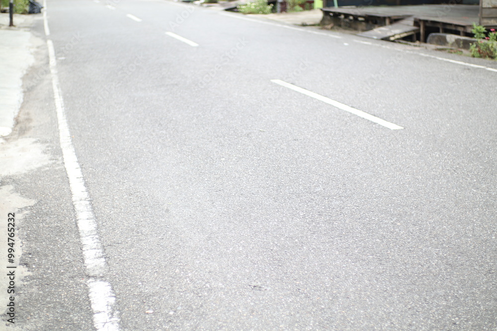 A long, empty asphalt road stretches into the distance. The road is lined with white lines and the sides are slightly unkempt. A long, empty asphalt road stretches into the distance. The road is lined with white lines and the sides are slightly unkempt.