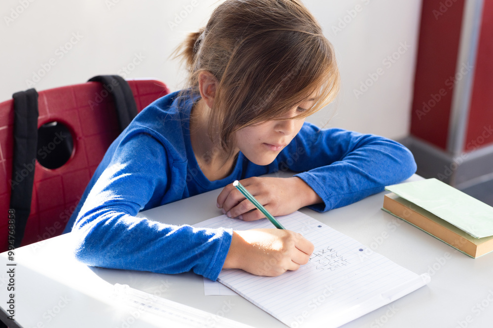 Naklejka premium In school, boy writing in notebook at desk, concentrating on homework